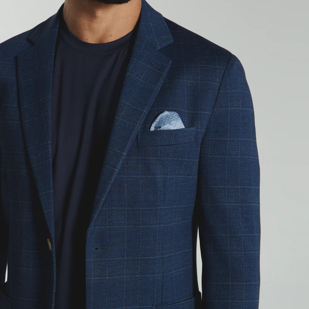 Man wearing a blue checkered suit jacket with a white pocket square on a gray background