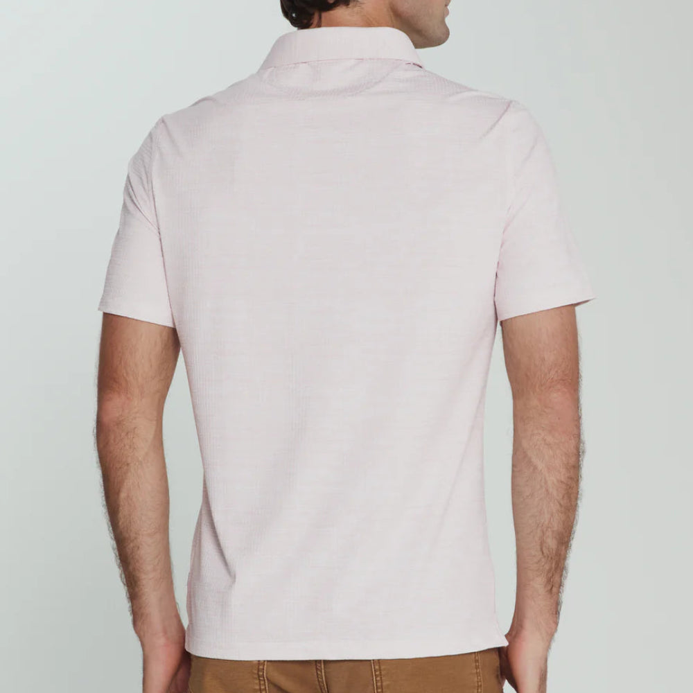 Man wearing a light pink polo shirt and brown pants on a white background