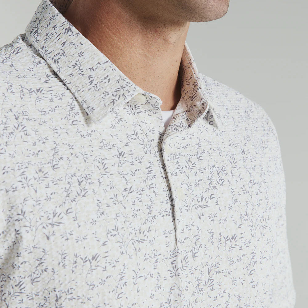 Close-up of a man wearing a white floral patterned shirt against a gray background