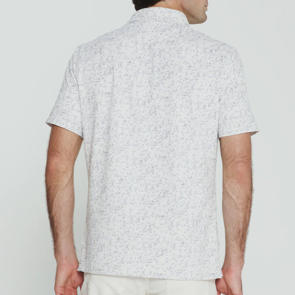 Man wearing a light gray patterned shirt and white pants against a plain background